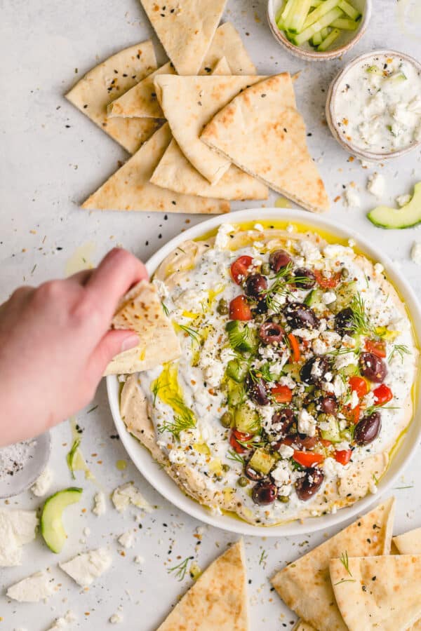 Greek Dip with Hummus and Tzatziki (134 calories) - a flavor-packed appetizer you can make a head of time! One layer of smooth, savory hummus, a layer of cool, herby tzatziki, and toppings like feta cheese, chopped fresh cucumbers, sweet tomatoes, and briney capers and olives.